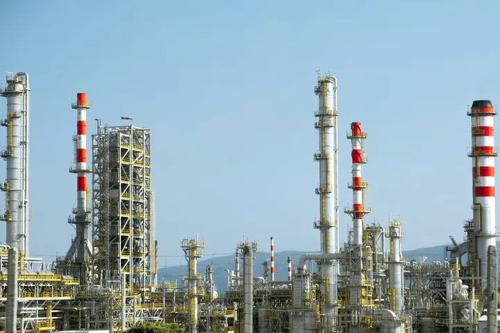 Refinery distillation columns and red and white stacks under a blue sky